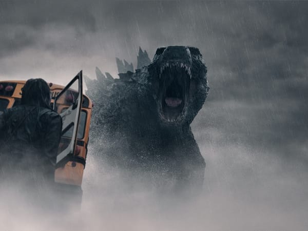 Godzilla in the rain with a bus turned over and woman looking up to Godzilla.